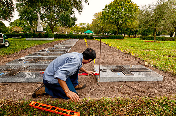 Nam Van Nguyen checks one of the refurbished memorials at the priests' burial section to ensure that is it properly aligned with the adjacent marker at the section south of the main outdoor altar at Calvary Catholic Cemetery.